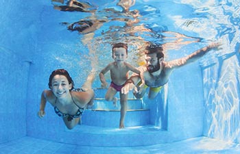 Happy family - father and mother with baby boy swimming and diving underwater with fun in blue pool.