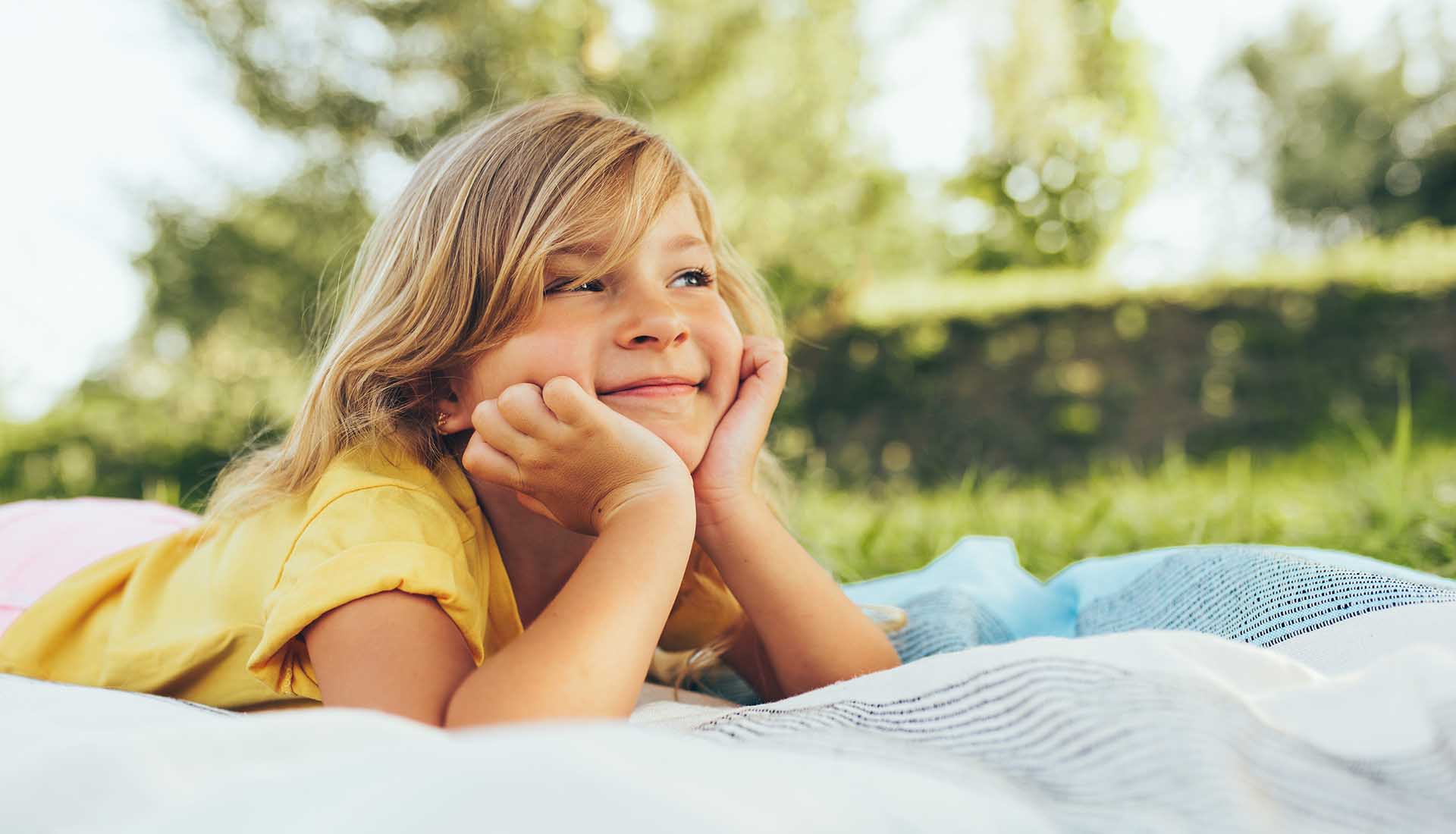 happy little girl laying on a blanket in a park