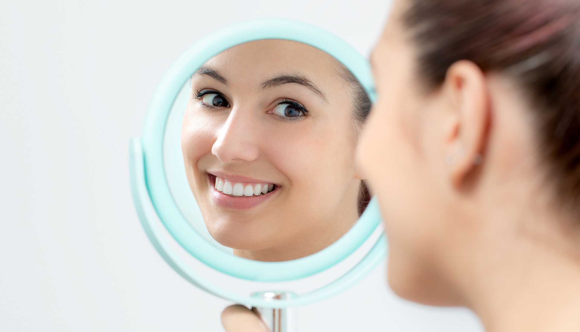 young woman looking at her perfect teeth in a mirror