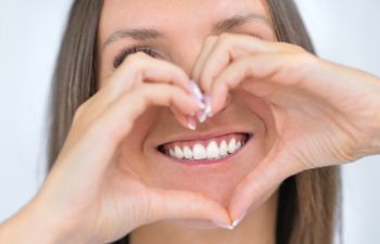 Smiling woman holding hands put in a shape of heart in front of her teeth.