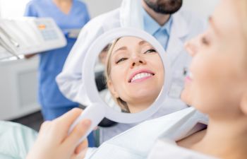 A woman dental patient looking at her perfect smile in a mirror.her